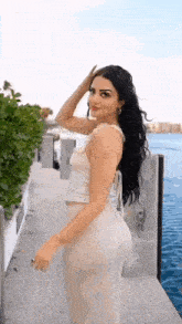 a woman in a white dress is standing on a pier near the water .