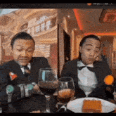 two men sitting at a table with wine glasses and a plate of food