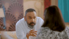 a man with a beard and a ring on his finger is talking to a woman on a couch