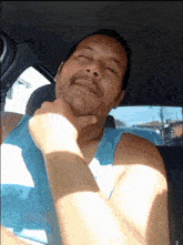 a man with a beard is sitting in a car with his eyes closed and his hand on his chin
