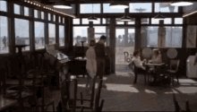 a group of people are sitting at tables in a restaurant with a lot of windows .