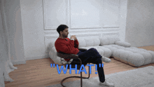 a man in a red sweater sits in a chair with the word " what " written in blue