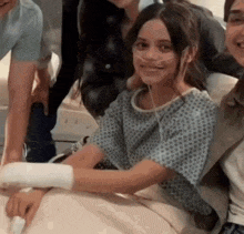 a girl in a hospital gown is sitting in a hospital bed with a bandaged arm .
