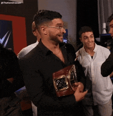 a man in a black suit holds a wrestling championship belt in his hands