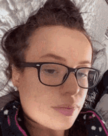 a woman wearing glasses is laying on a bed and making a funny face .