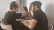 a man scratches his head while another looks at his phone