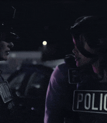 a police officer is talking to another officer who is wearing a black vest that says police on it