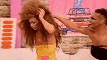 a man is holding a woman 's hair while a woman in a yellow dress looks on .