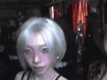 a woman with white hair and blue eyes is standing in a dark room .
