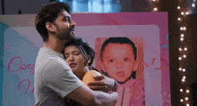 a man and a woman are hugging in front of a picture of a child .