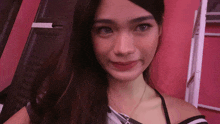 a woman with a necklace around her neck looks at the camera in front of a pink wall
