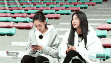 two girls are sitting in front of a row of bleachers and one of them is using her phone