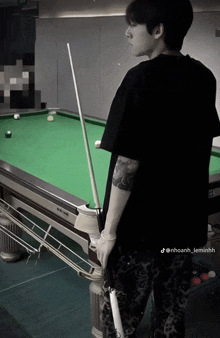 a man with a tattoo on his arm is standing in front of a pool table holding a pool cue