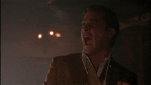 a man in a brown suit and white shirt is laughing with his mouth open