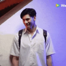 a man wearing a white shirt and a black backpack is standing in front of a wall .