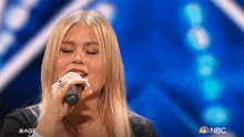 a woman is singing into a microphone on nbc 's america 's got talent