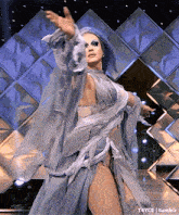 a drag queen with purple hair is dancing on a stage in front of a mirrored wall .
