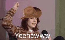 a woman wearing a cowboy hat and sweater is holding a microphone .