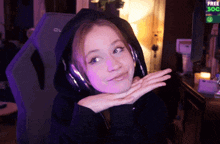 a girl wearing headphones and a hoodie looks at the camera with a sign in the background that says free soc