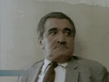 a man in a suit and tie is leaning against a wall with his eyes closed