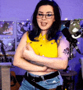 a woman wearing glasses and a yellow shirt is standing with her arms crossed