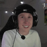 a young man wearing headphones and a hat is smiling while sitting in a chair .