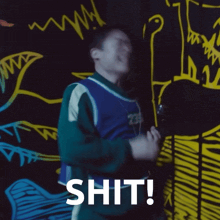 a man is standing in front of a wall with drawings on it and the word shit written on it