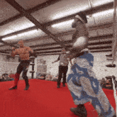 a referee watches two wrestlers in a ring with one wearing blue and white pants