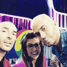 two men and a woman pose for a picture in front of a rainbow