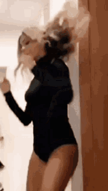 a woman in a black bodysuit is dancing in a room while holding a cup .