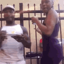 a man and a woman are dancing in front of a fence . the woman is wearing a purple dress .
