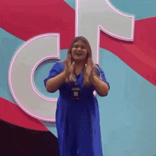 a woman in a blue dress is clapping her hands in front of a tik tok logo .