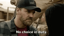 a man with a beard wearing a hat is talking to a woman and saying `` no choice in duty '' .