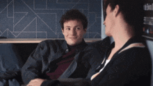 a man and a woman are sitting on a couch and the man is wearing a black jacket