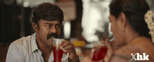 a man with a mustache is drinking from a glass while talking to a woman