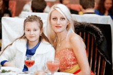 a woman and a little girl sit at a table with glasses of wine