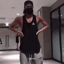 a man wearing a black adidas tank top stands in a gym with his hands on his hips