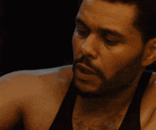 a man with a beard and a black tank top looks at something