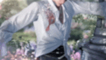 a man in a suit and tie is standing in a garden with his arms outstretched and flowers in the background .