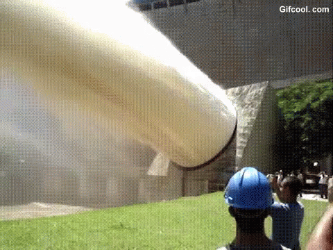 a man wearing a blue hard hat is taking a picture of a large pipe .