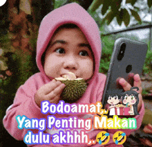 a little girl is eating a durian while holding a phone