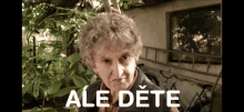 an older woman stands in front of a tree with ale dete written on the bottom of her face