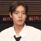 a man in a white shirt and tie is standing in front of a netflix sign