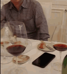 a man sits at a table with wine glasses and a phone
