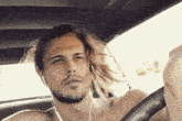 a shirtless man with long hair and a beard is sitting in a car with headphones on .