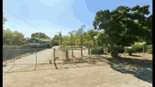 a fence surrounds a dirt road with a house in the distance