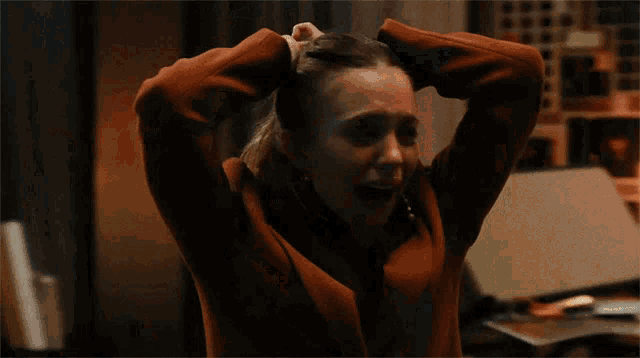 a woman in a red jacket is holding her head in her hands .