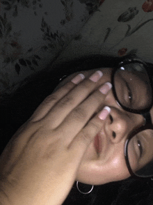a woman wearing glasses covers her face with her hand