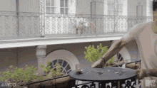 a man is standing on a balcony next to a table with a cup on it .