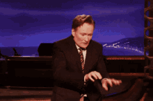 a man in a suit and tie is sitting on a stage with his arms outstretched